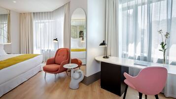 Una habitación de hotel moderna con una cama, dos sillas, un escritorio y un ventanal con cortinas.