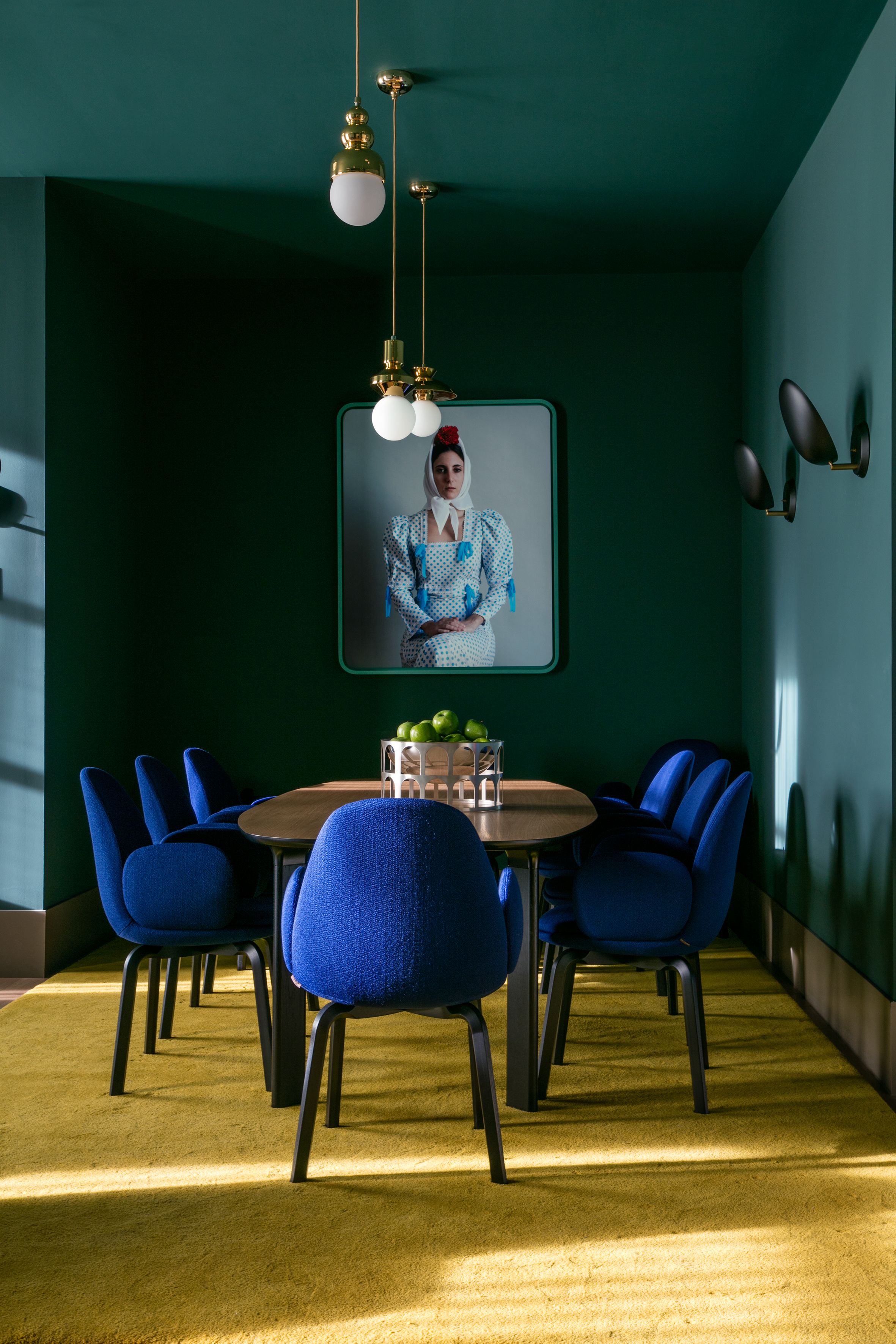 A conference room with a round table, blue chairs, and a framed portrait on the wall.