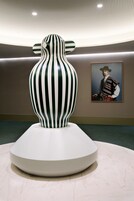 Una escultura moderna con franjas verticales sobre un pedestal en una galería.