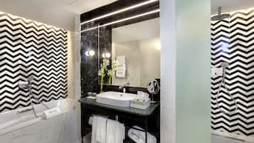Un baño moderno con una pared de diseño en blanco y negro con patrón de espiga, un lavabo blanco, un espejo grande, un cabezal de ducha de mano y una bañera.