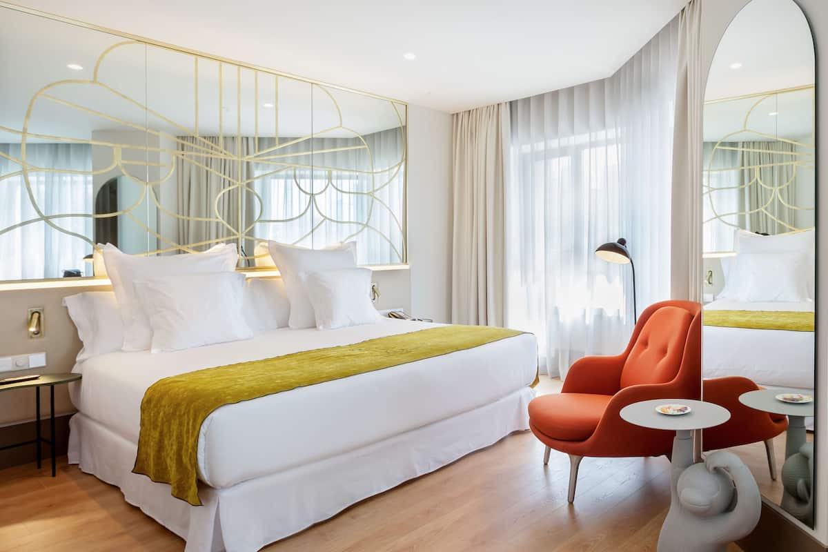 Una habitación de hotel moderna con una cama grande, un ventanal luminoso, un escritorio y una silla.