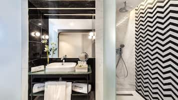 Un baño moderno con un espejo grande, un lavabo y una ducha. Hay toallas y una pequeña cesta en la encimera.