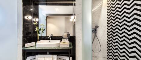 Un baño moderno con un espejo grande, un lavabo y una ducha. Hay toallas y una pequeña cesta en la encimera.