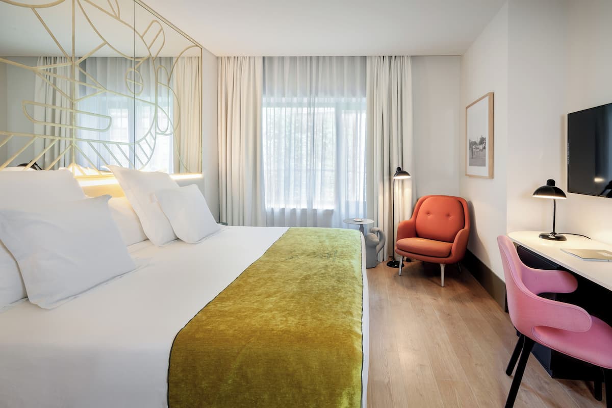 Habitación de hotel con cama, escritorio, silla, televisión y ventana con cortinas.