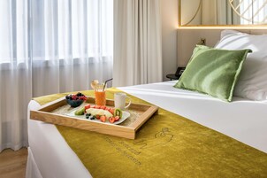 Una camera d'albergo con un letto, un vassoio per la colazione con frutta e succo di frutta, un cuscino verde e un comodino a parete.