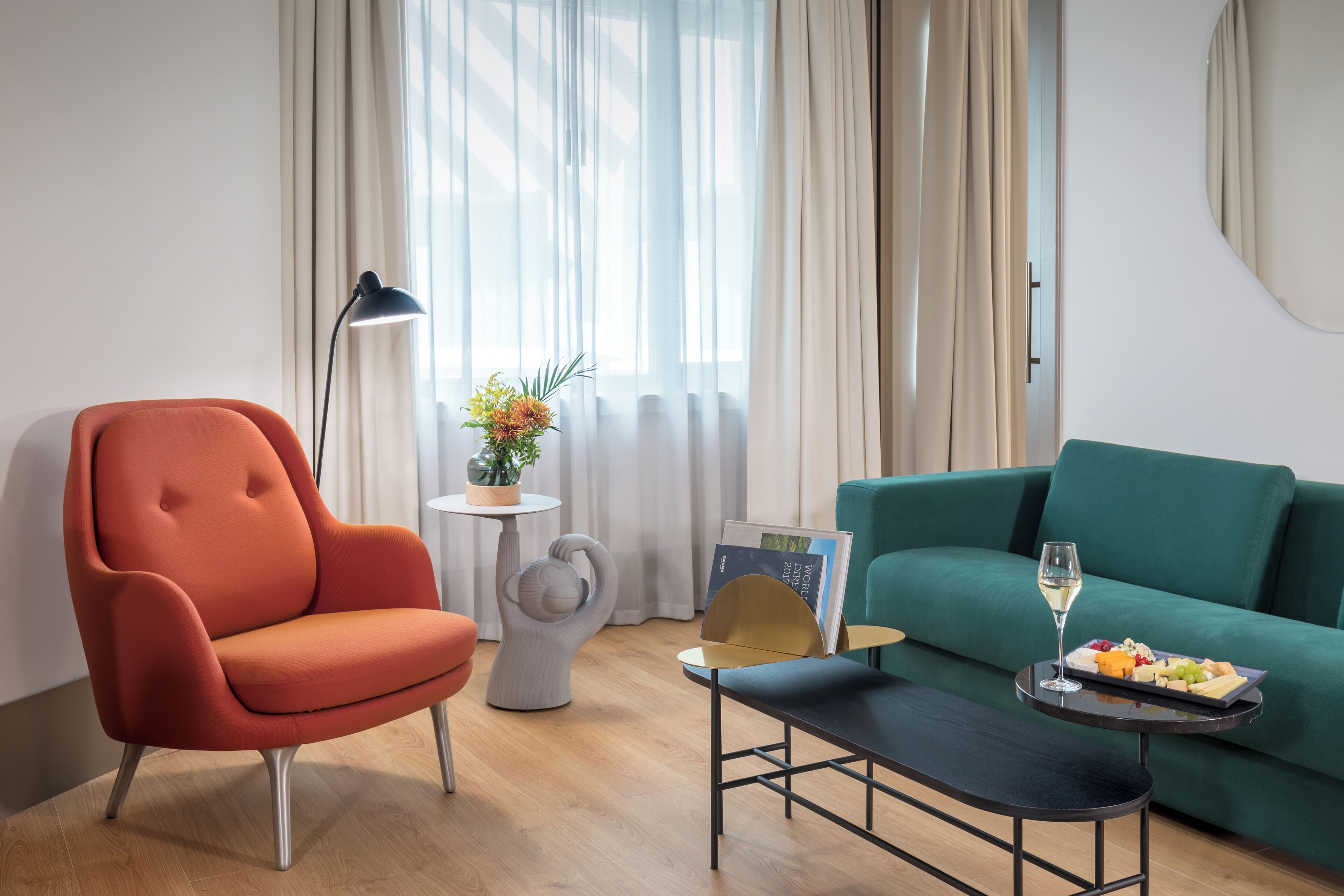 Una sala de estar moderna con un sillón rojo, un sofá color turquesa, una mesa de centro con una copa de vino y fruta, y una lámpara.