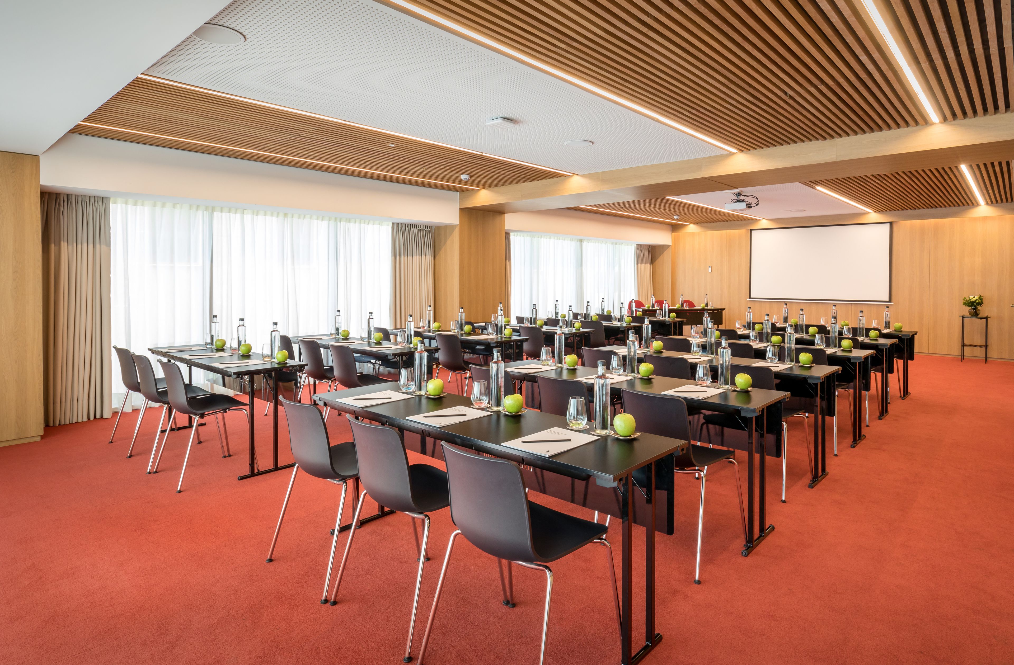 A conference room with multiple tables, chairs, and a large screen.
