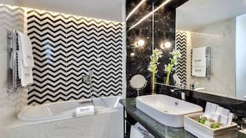 A modern bathroom with a zigzag patterned wall, a large mirror, a bathtub, and a sink with toiletries.