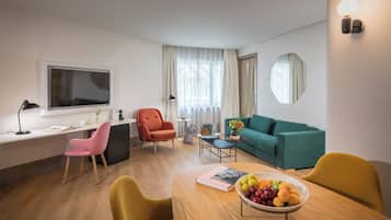 Una sala de estar moderna con un sofá, una mesa de comedor con un frutero, un escritorio con una computadora y un televisor.