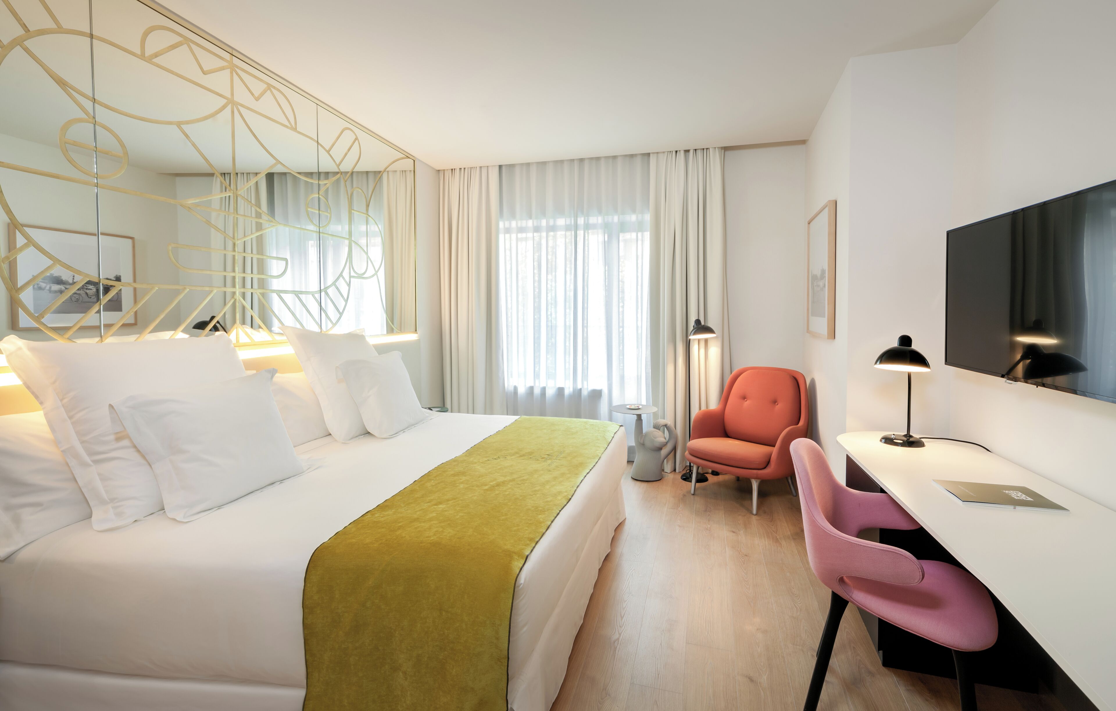 A hotel room with a bed, a desk, a chair, a TV, and a window with curtains.
