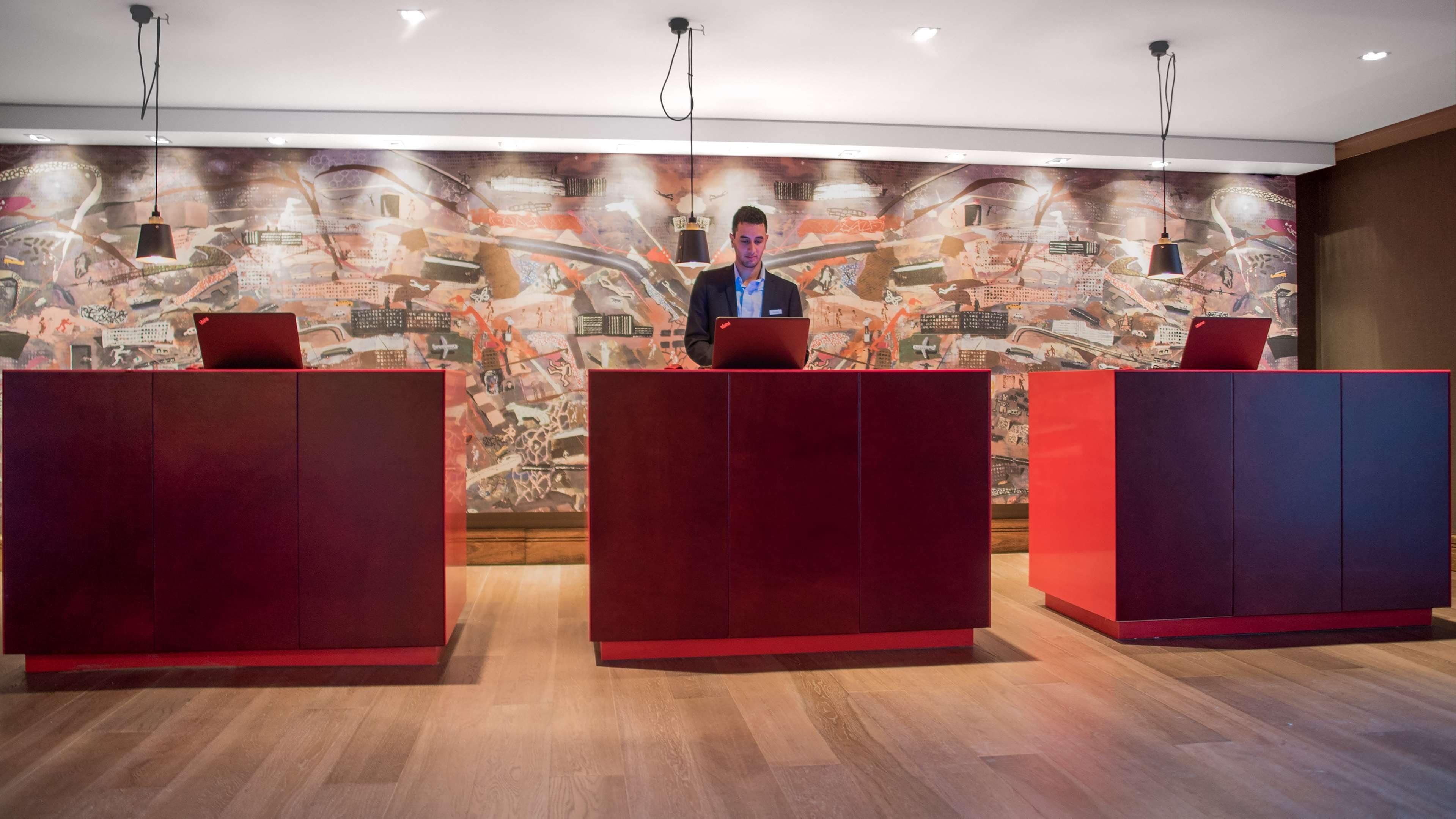 Un área de recepción con tres mostradores rojos y un mural moderno y abstracto de fondo.