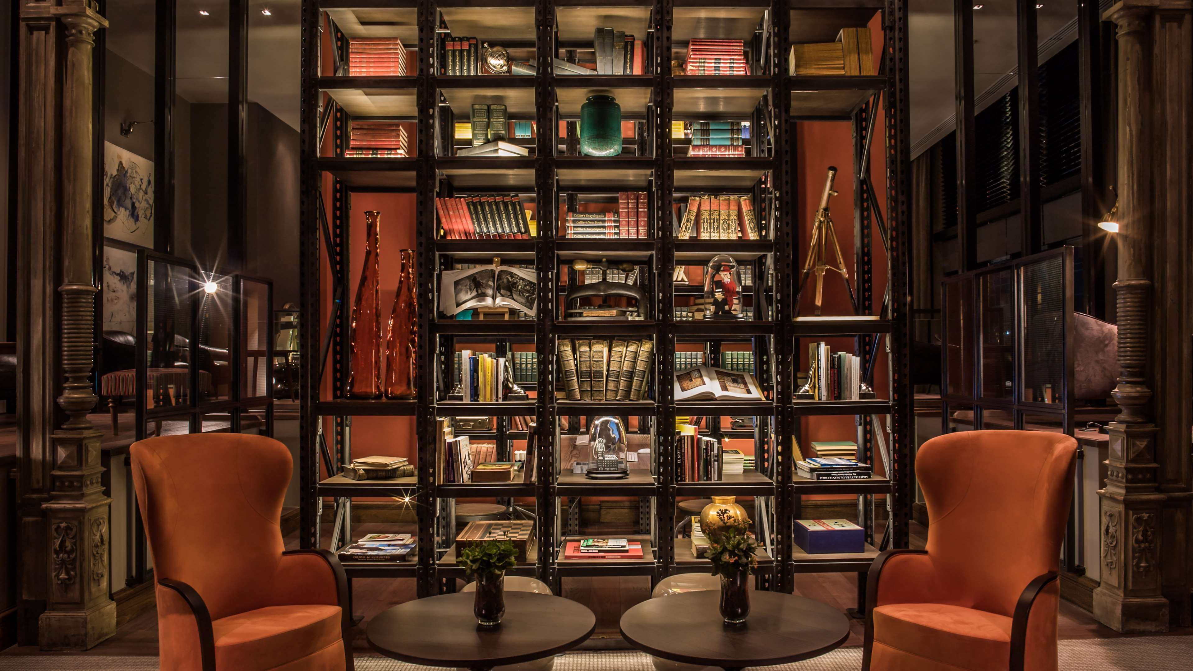 A library with bookshelves filled with books and decorative items. There are two round tables with chairs in front.