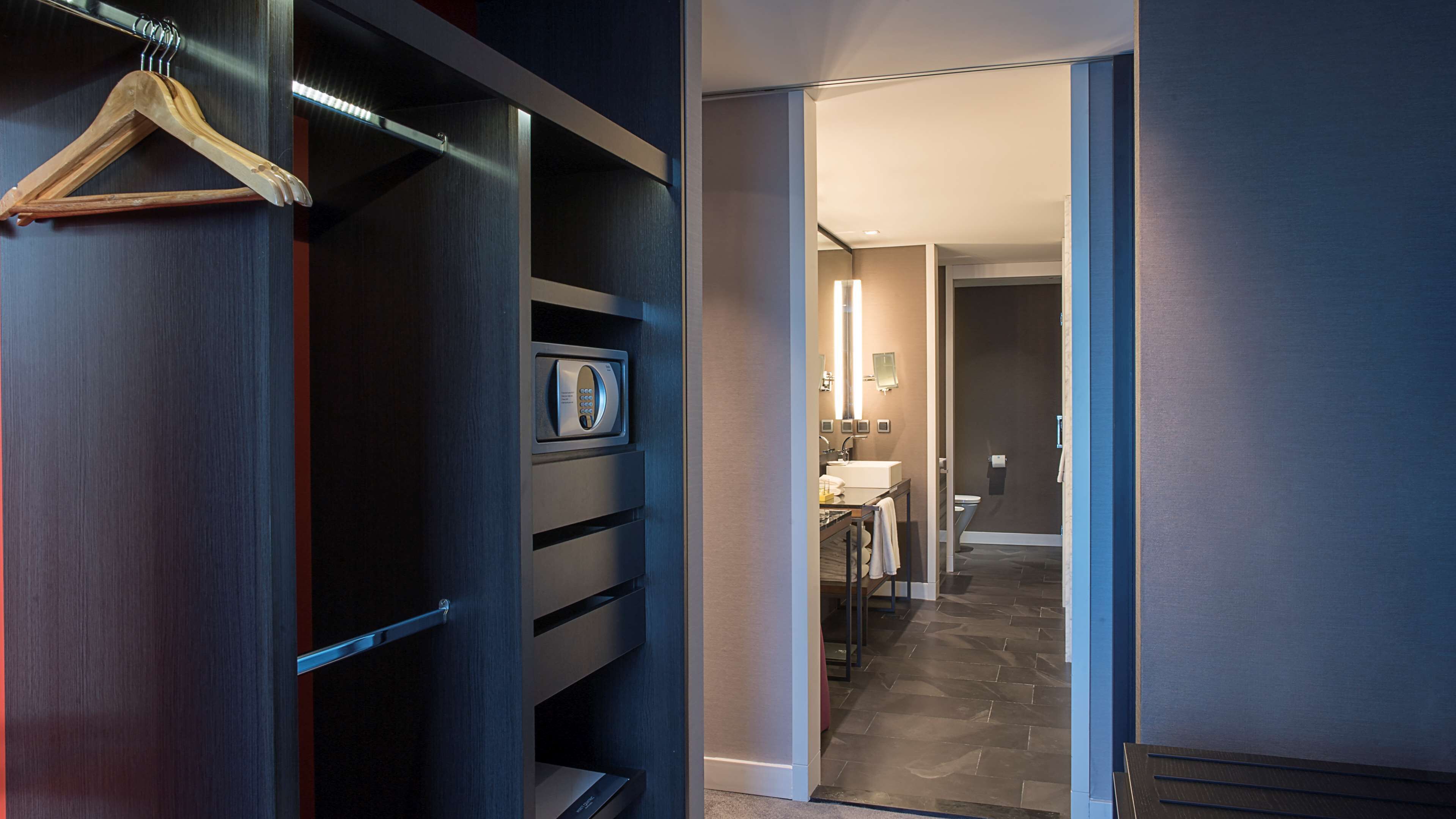 A hotel room with a walk-in closet, a bathroom with a shower, and a small sitting area.