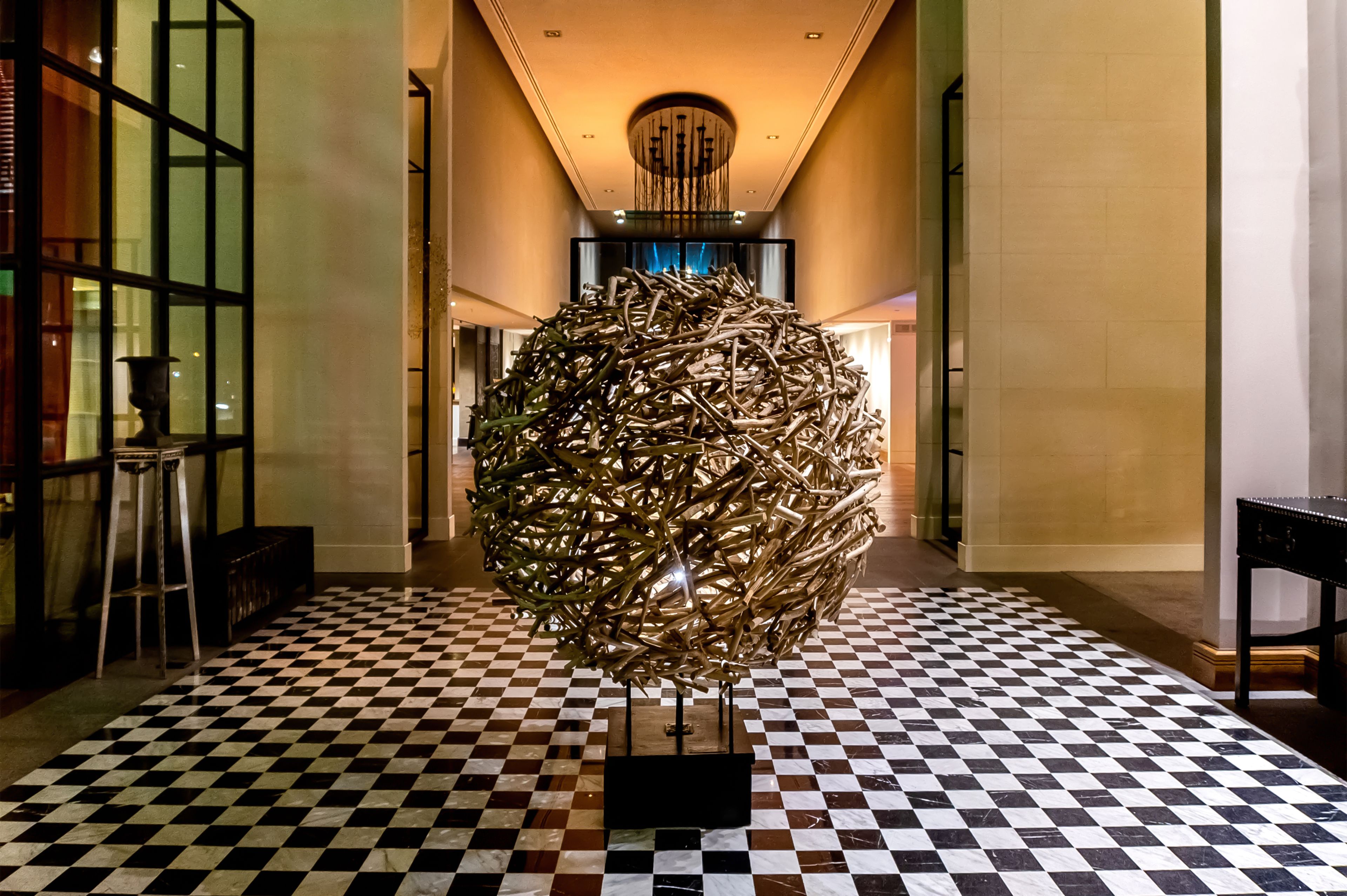 A lobby with a checkered floor, a large metallic sculpture, and a staircase in the background.