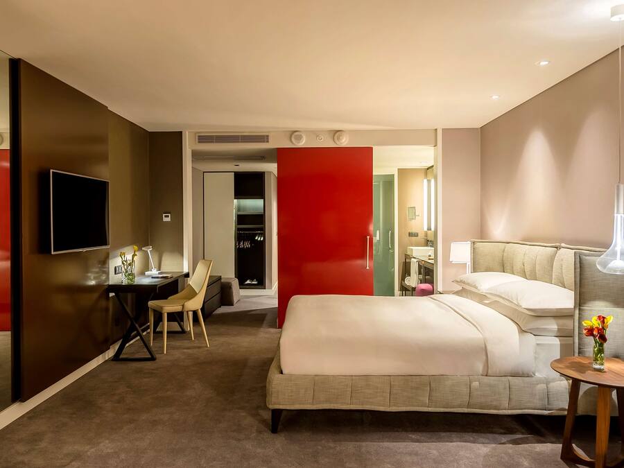 Habitación de hotel moderna con una cama grande, un escritorio con silla, un televisor y una pared decorada en color rojo.