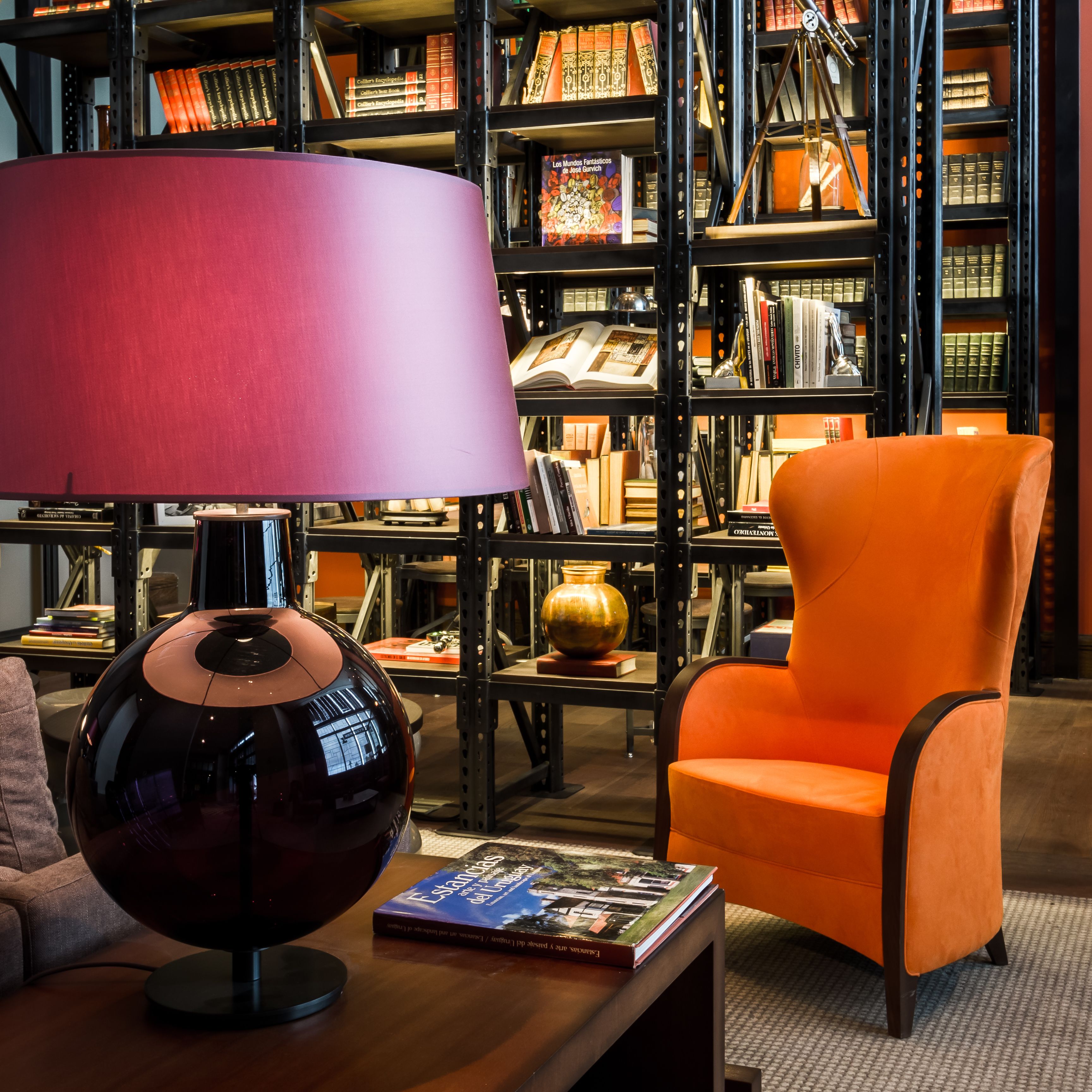 Een bibliotheek met boekenkasten, een wereldbol, een lamp en een oranje fauteuil.