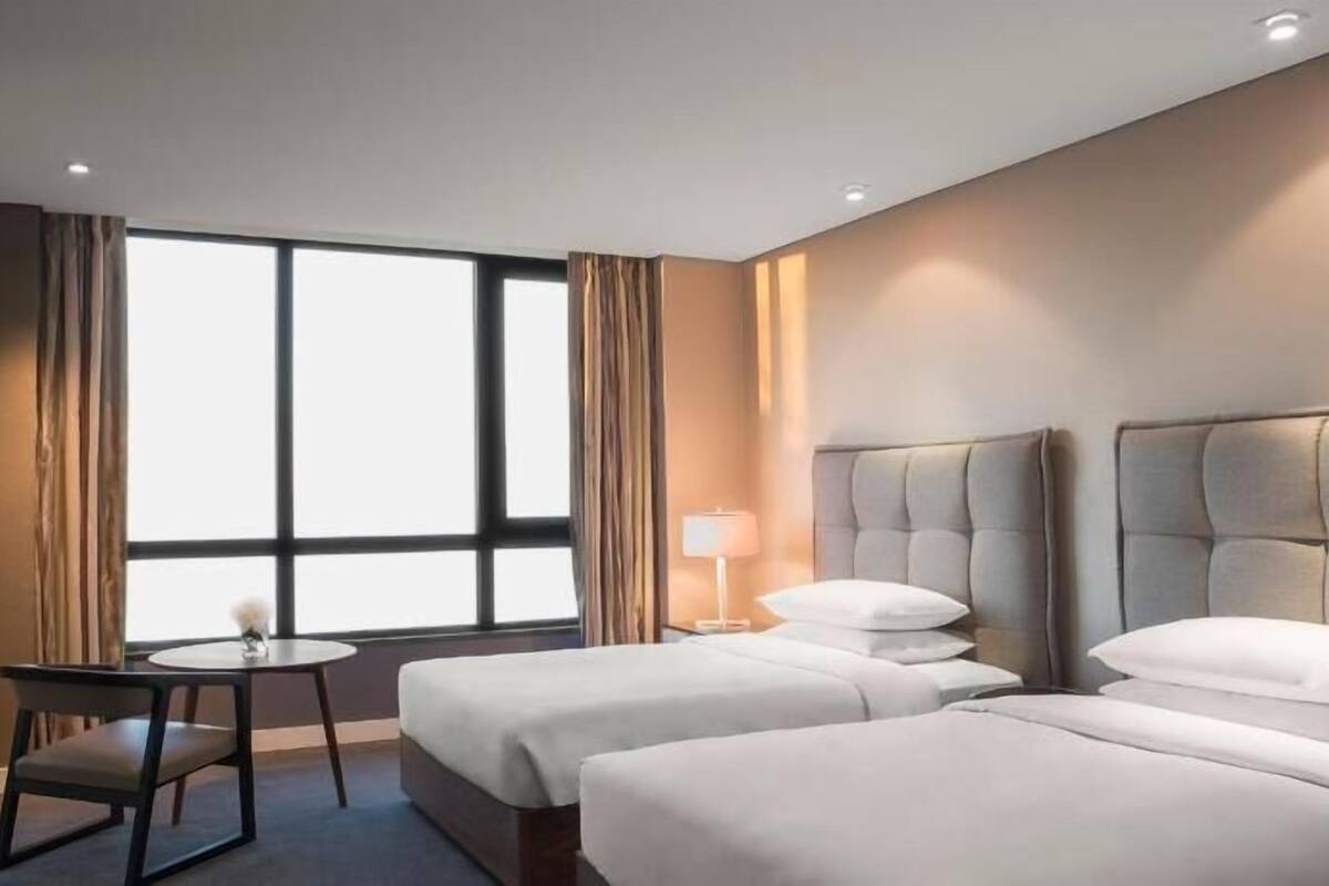 Une chambre d’hôtel avec deux lits, une petite table, une chaise, un téléviseur et une fenêtre avec des rideaux.