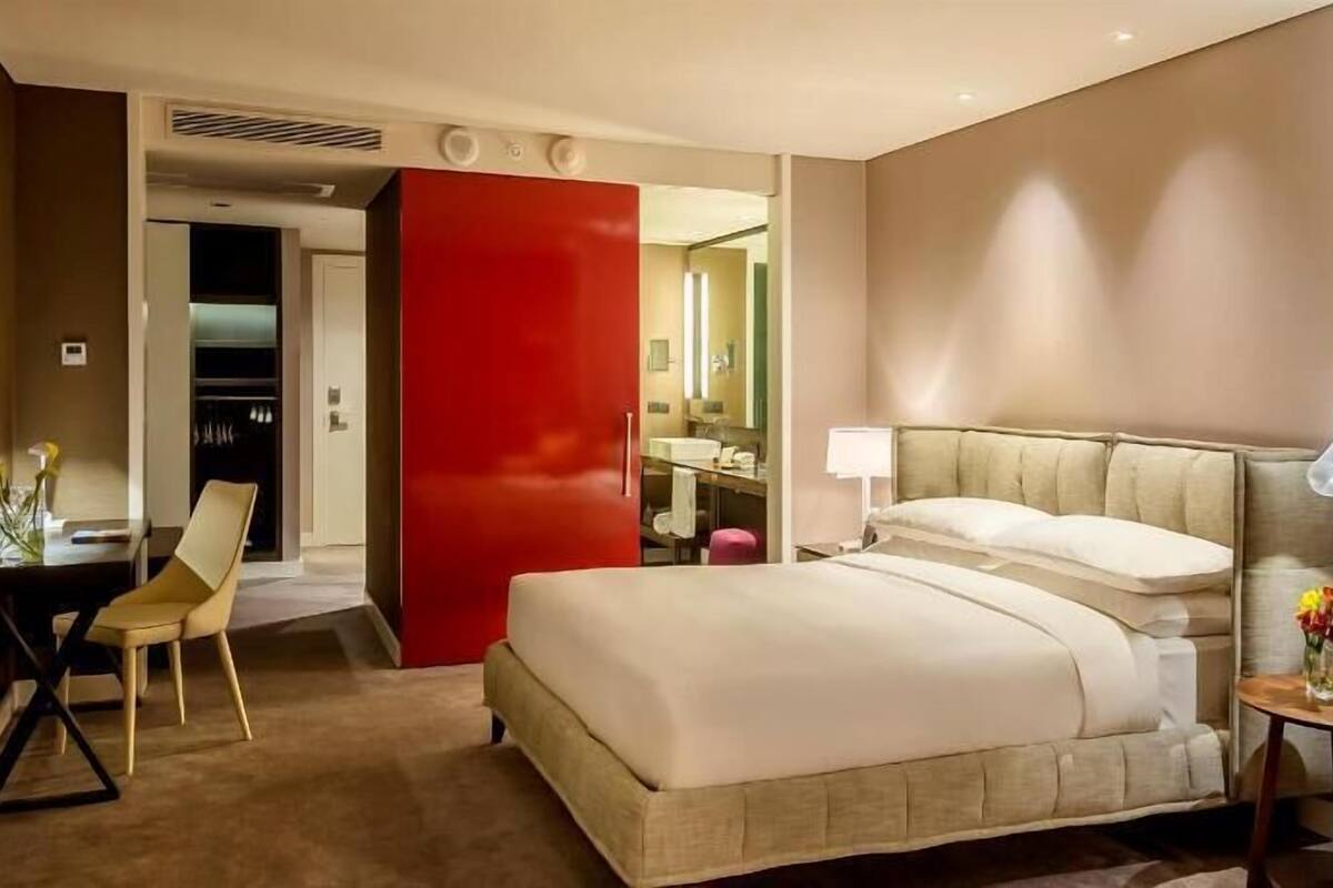Une chambre d’hôtel avec un lit, un bureau, une chaise, une petite table avec un vase et un mur d’accent rouge.