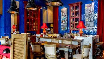 Zona de bar con mobiliario de madera, lámparas colgantes rojas y negras, y una barra con una variedad de botellas.