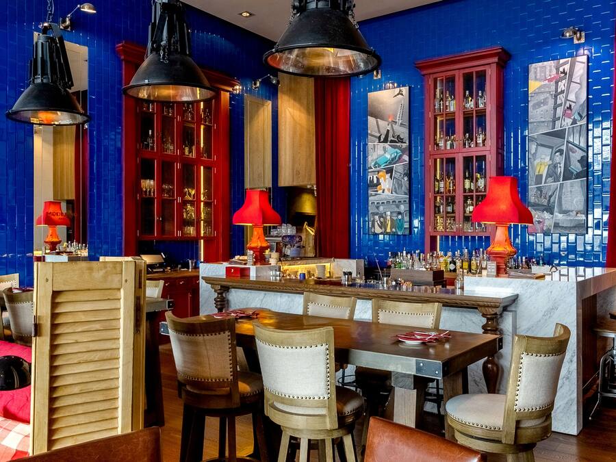 Zona de bar con mobiliario de madera, lámparas colgantes rojas y negras, y una barra con una variedad de botellas.