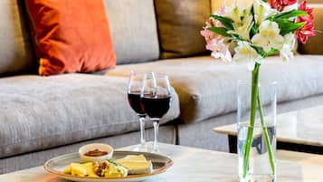 Una mesa de comedor con un plato de queso y frutos secos, dos copas de vino tinto y un florero con flores.