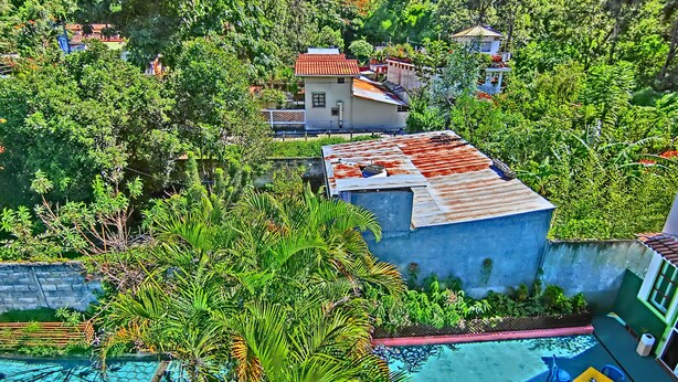 A resort with a swimming pool, surrounded by lush greenery and multiple buildings with red-tiled roofs. - Hotel El Sol (Panajachel)