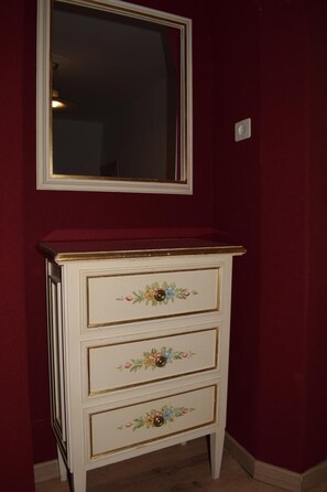 A white dresser with floral designs, a mirror above it, and a red wall.