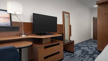 Habitación de hotel con escritorio de madera, televisor de pantalla plana, espejo, silla azul y armario.