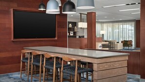 A modern bar area with a large flat-screen TV, wooden bar stools, pendant lighting, and a marble countertop. - Fairfield Inn & Suites by Marriott Panama City Beach (Panama City Beach)