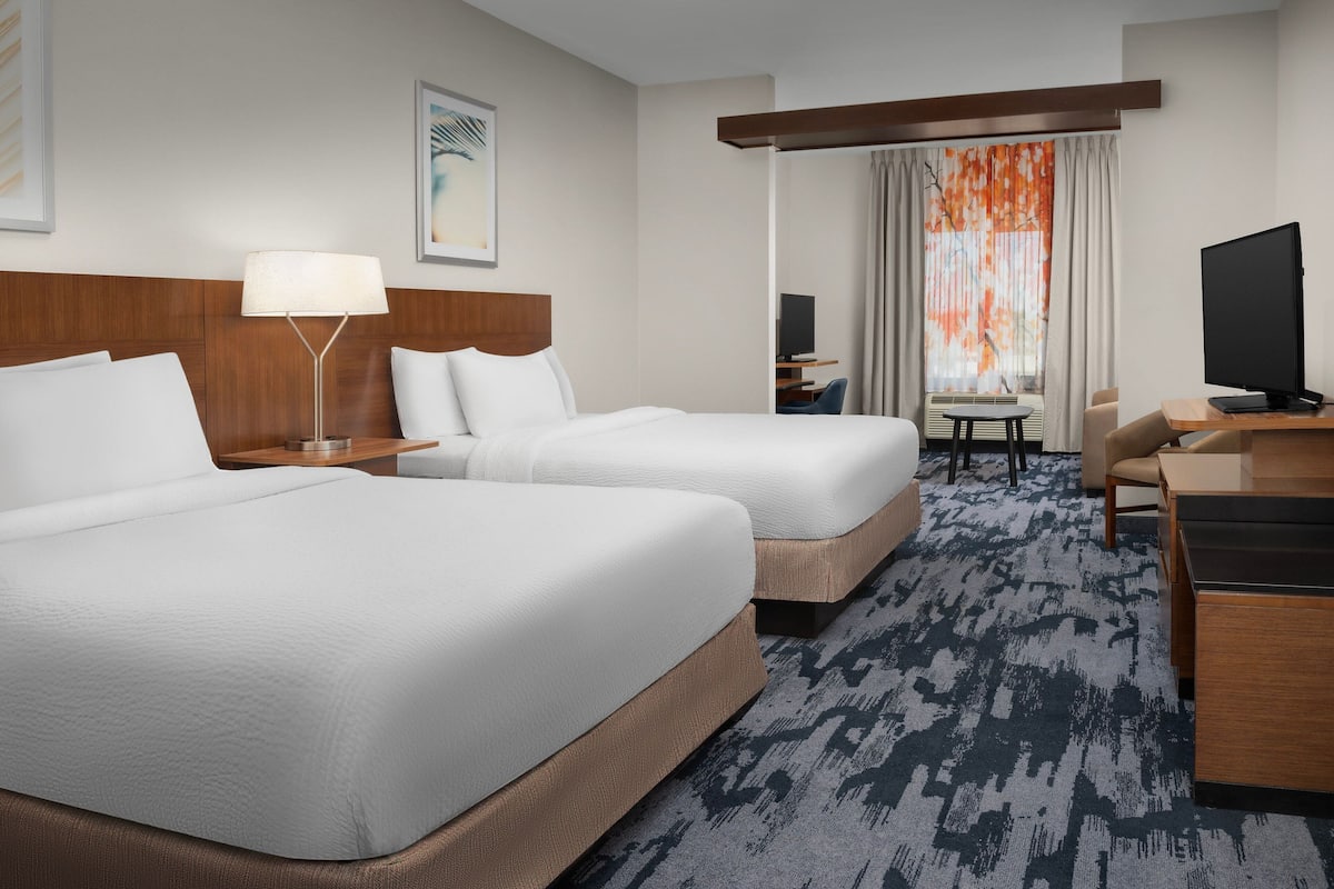 A hotel room with two beds, a desk, a chair, a television, and a window with curtains.