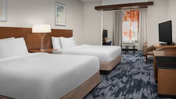 A hotel room with two beds, a desk, a chair, a television, and a window with curtains.