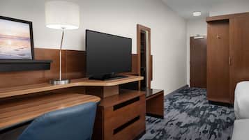 Una habitación de hotel con un escritorio de madera, un televisor de pantalla plana, una lámpara, un armario y una silla azul.