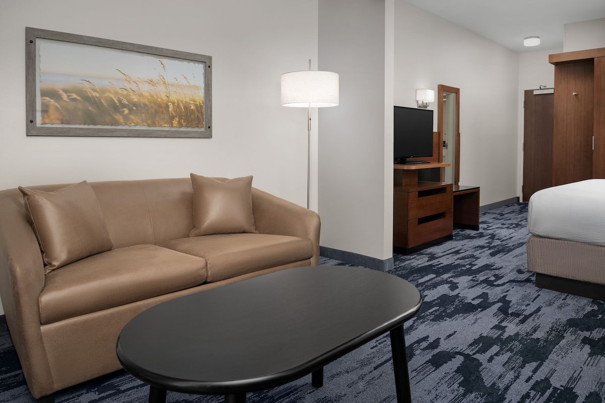 A hotel room with a beige sofa, a small table, a TV on a wooden stand, a mirror, and a wardrobe.