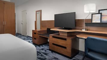 A hotel room with a bed, a desk with a computer, a chair, a TV, and a lamp.