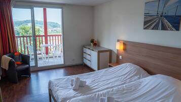 Habitación de hotel con cama, escritorio, silla, una mesita y balcón con vista al mar.