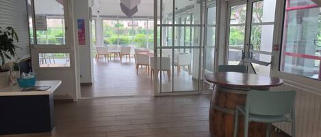 An open-plan office space with a wooden floor, a bar area with a wooden barrel, and a view of an outdoor seating area with white chairs.
