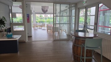 An open-plan office space with a wooden floor, a bar area with a wooden barrel, and a view of an outdoor seating area with white chairs.