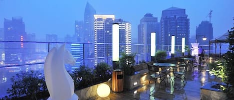Una terraza en la azotea con vista al horizonte urbano, mobiliario exterior y una estatua decorativa de un caballo.