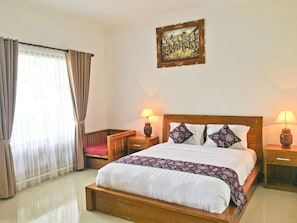 Una habitación de hotel con una cama grande, dos lámparas de noche, un cabecero de madera, un cuadro en la pared y una ventana con cortinas.