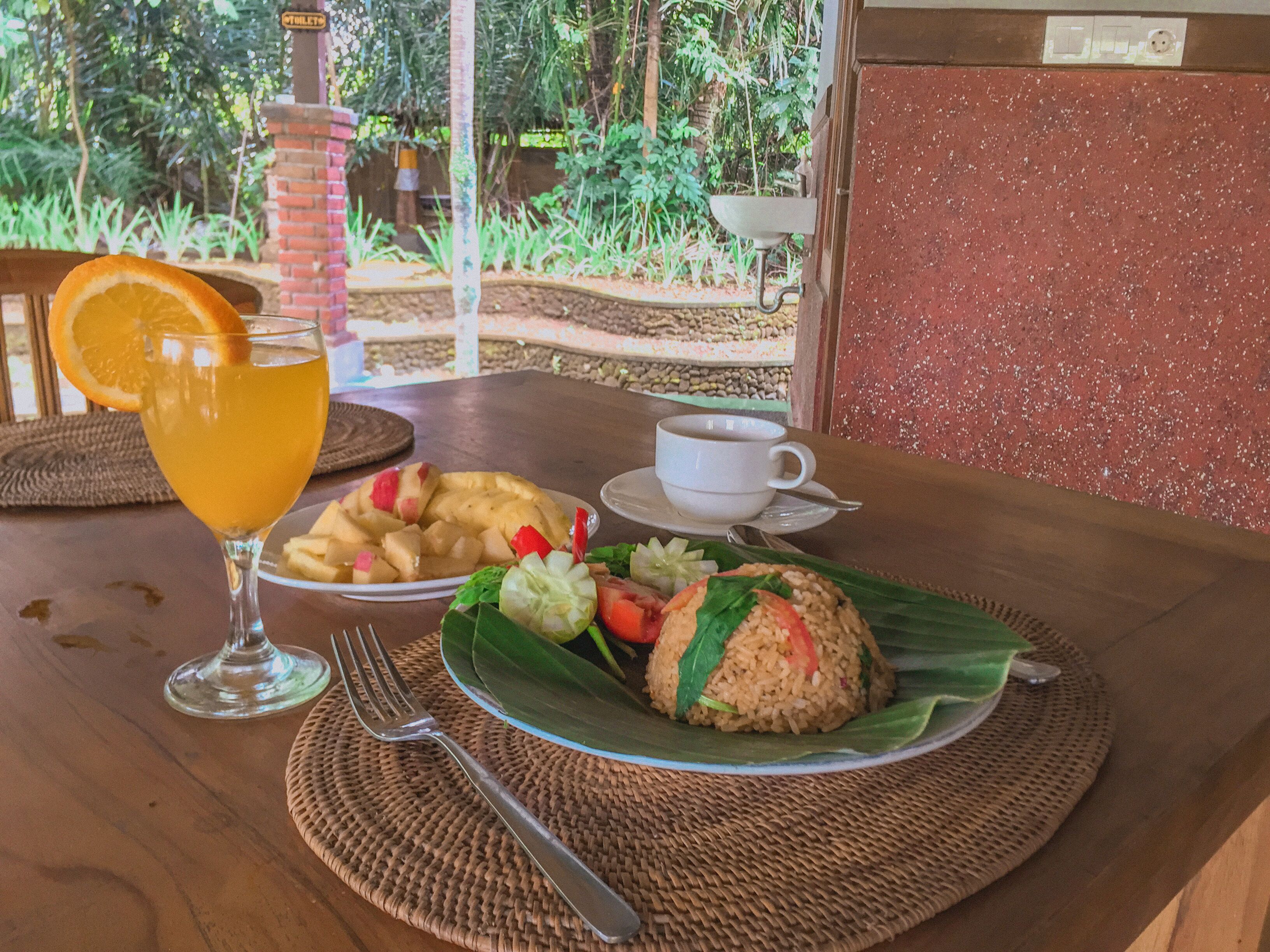 A table with a glass of orange juice, a cup of coffee, a plate of fruit, and a wrapped rice dish.