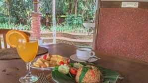 Una mesa con un vaso de jugo de naranja, una taza de café, un plato de fruta y un plato de arroz envuelto.