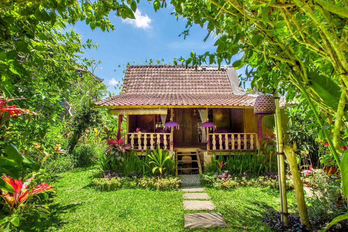 A traditional house with a tiled roof, surrounded by lush greenery and a stone pathway leading to the entrance.