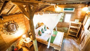 A wooden room with a bed, a mirror, a small table with a lamp, and a sign on the wall. - Swasti Eco Cottages (Ubud)
