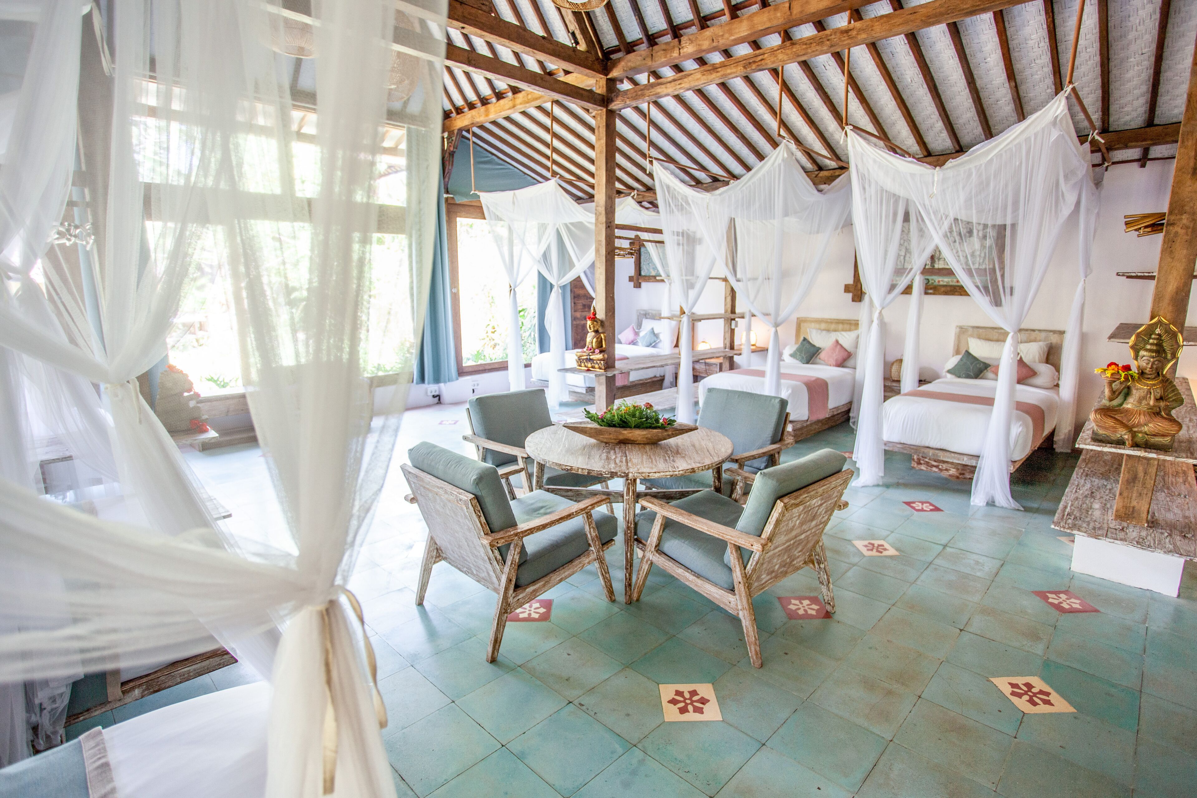 A room with a round table, four chairs, and a bed with white canopy beds.