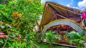 A thatched-roof structure with a checkered awning, surrounded by lush greenery and a stone pathway. - Swasti Eco Cottages (Ubud)