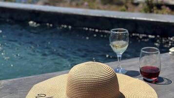 A straw hat with "Enjoy your vacation" written on it, two wine glasses, one with white wine and the other with red wine, and a view of a coastal town with buildings and a body of water.
