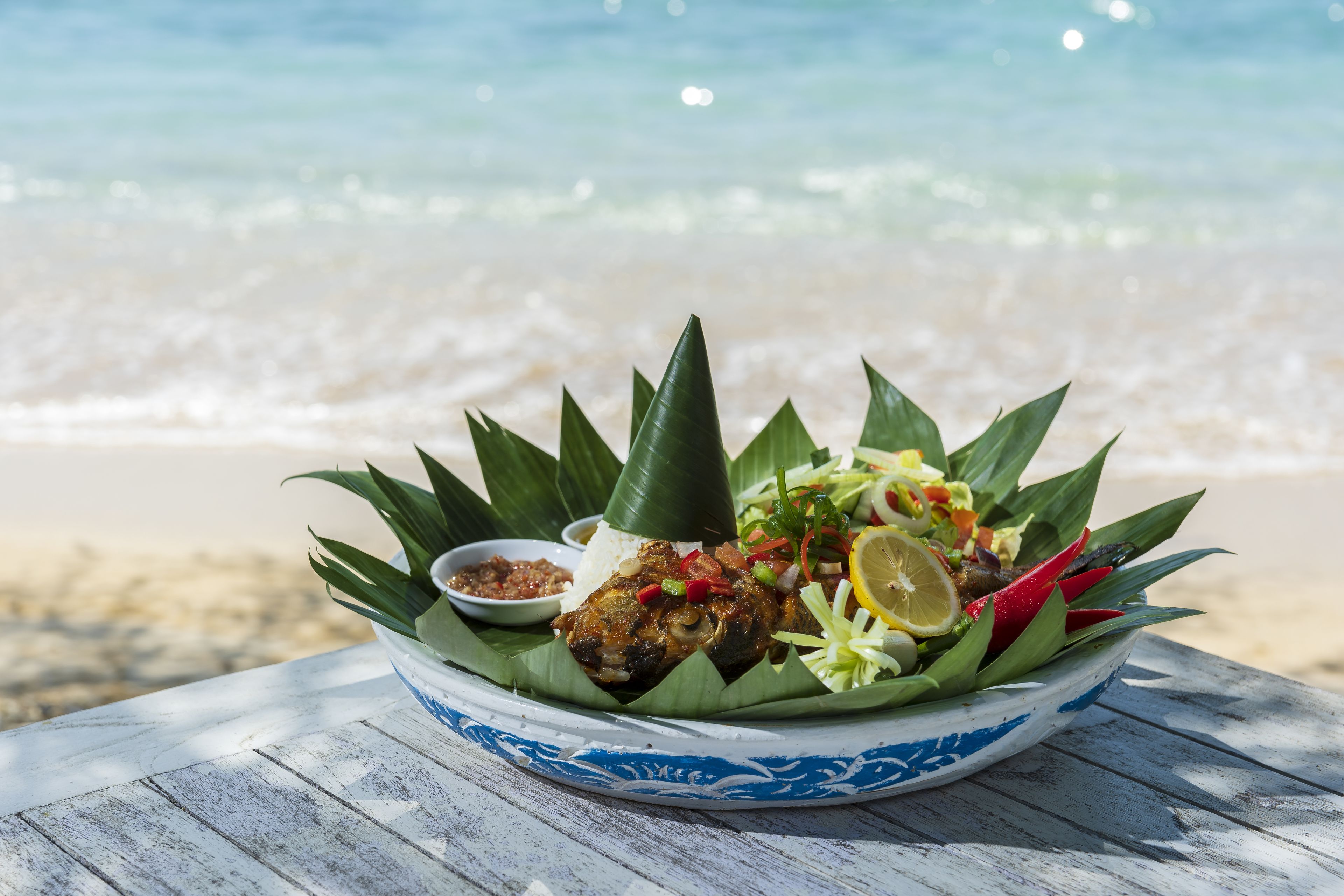 Una comida sobre una mesa de madera junto a la playa.