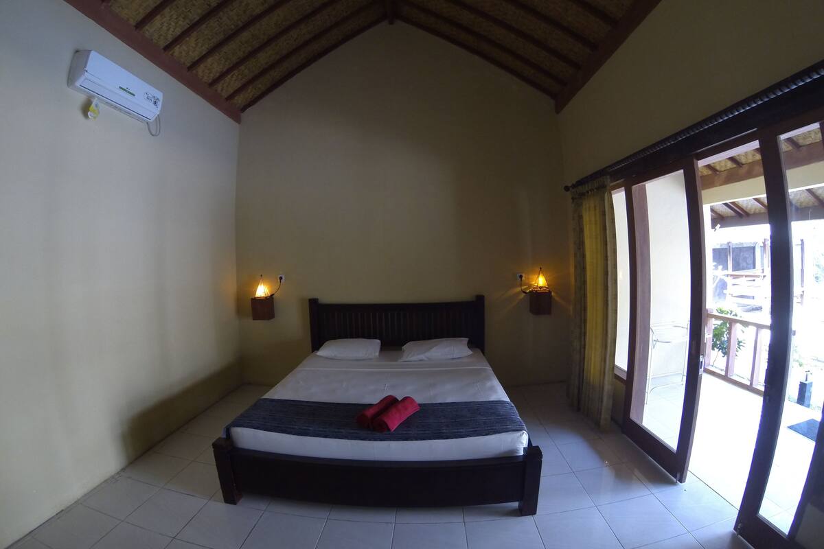 Quarto com cama, duas luminárias na parede, ventoinha no teto e janela com vista para o exterior.