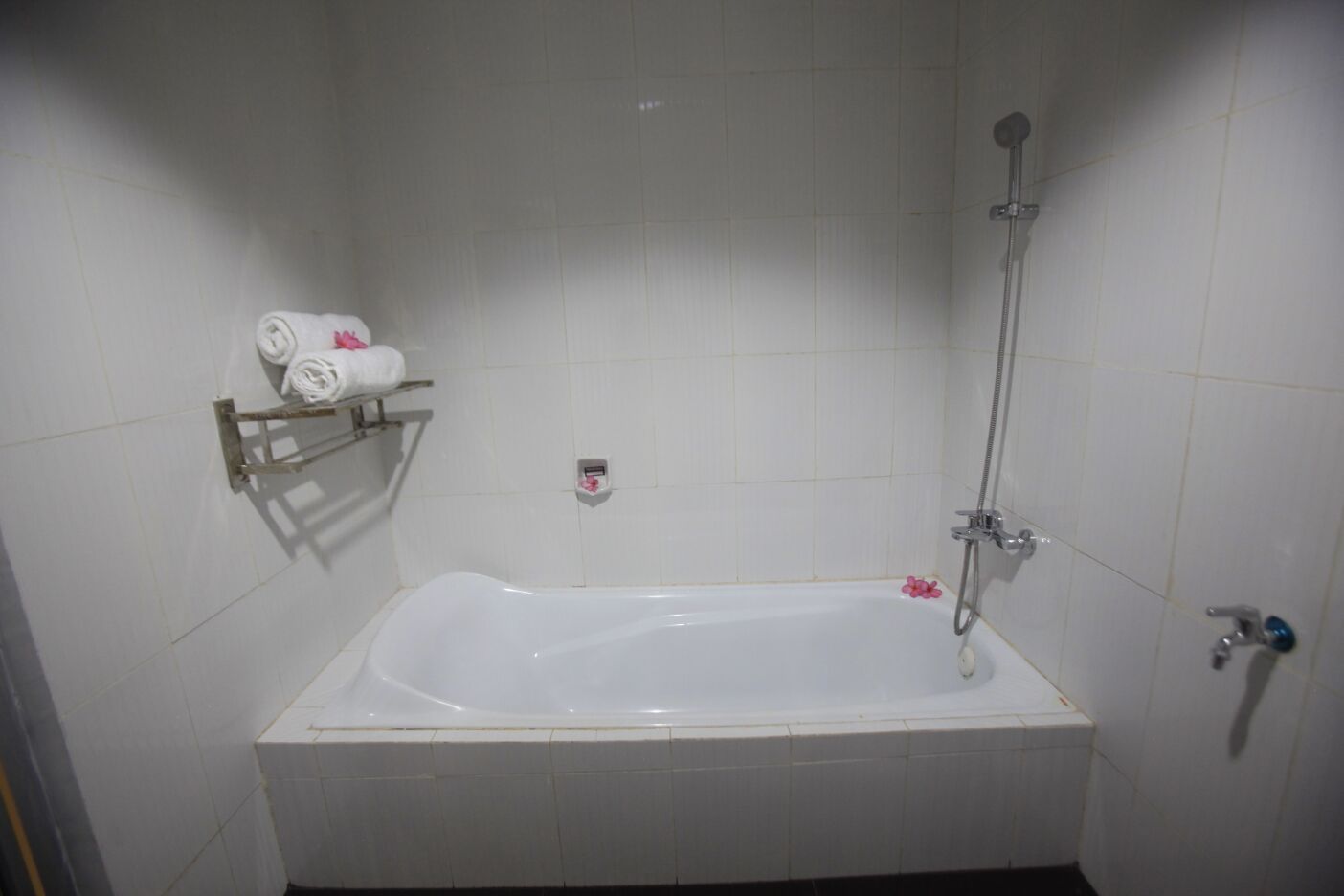 Une salle de bain standard aux murs recouverts de carreaux blancs, équipée d’une baignoire, d’une douche, d’un porte-serviettes et d’un distributeur de savon.