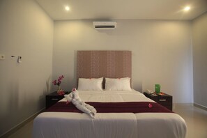 Quarto de hotel com uma cama grande, uma mesa de cabeceira com telefone e uma caixa verde, e ar-condicionado fixado na parede.